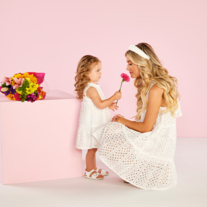 A mom and daughter wearing matching white eyelet dresses, holding a flower